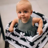 A baby in a gray sleeveless outfit is sitting inside a Milk Snob basket, featuring the Cover Disneys Mickey Mouse design. The multifunctional cover adds charm as the little one gazes up curiously, exploring their world.