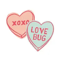 Two heart-shaped candies use eco-friendly dyes: pink with XOXO in red and light blue featuring Finn and Emmas Organic Tee, Love Bug theme.