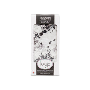 Lulujo Inc.s Bamboo Swaddle with a black floral design is packaged in a windowed box.