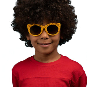 A child with curly hair wears Sunstaches Arkaid Sunglasses in Spongebob Pineapple style, red shirt, smiling on a white background.