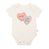 This Valentines Day, dress your baby in Finn and Emmas Organic Bodysuit, Love Bug. Made of soft organic cotton, it features a white design with two hearts: a pink XOXO and a blue LOVE BUG, offering style and comfort for their special day.