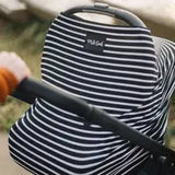 A close-up of a baby stroller features the Milk Snob Cover Modern Stripe nursing cover. A hand in an orange sleeve grasps the handle as the multifunctional cover fits snugly, framed by blurry greenery and a path.