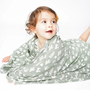 A toddler smiles, wrapped in Emerson and Friends Stay Sharp bamboo blanket featuring a cactus print.