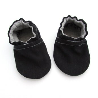 The Cabooties, Denim Black baby shoes feature ruffled elastic openings and stitched detailing with grippy soles, displayed on a white background.