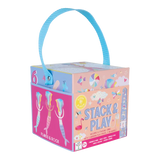 The Floss and Rock Stack and Play, Fantasy is a colorful cube-shaped toy box with whimsical clouds, rainbows, and unicorns design. Featuring a blue handle and suitable for ages 2+, it includes 10 uniquely designed wooden pieces.