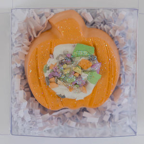 Hopscotchs Sidewalk Chalk, Pumpkin-shaped with bright hues and sprinkles, in a clear box with shredded white paper.