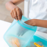 A hand puts orange slices into a Bumkins blue silicone bag with child-friendly zip, ideal for an eco-friendly kitchen.