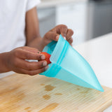 Hands place a strawberry into a Bumkins Silicone Flat Reusable Bag over a wooden cutting board.