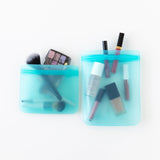 The Bumkins Silicone Flat Reusable Bag 2 Pack in blue holds makeup essentials—brushes, lipsticks, and an eyeshadow palette.