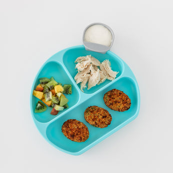 A Bumkins Silicone Grip Dish: Blue holds chicken, fruit salad, and falafel on a food-safe silicone surface against a white background.