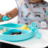 A child uses a spoon to eat from the Bumkins Silicone Grip Dish: Blue, made of food-safe silicone with a strong suction base on the highchair.