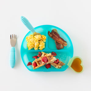 Bumkins Silicone Grip Dish: Blue Jelly features divided sections with scrambled eggs and a fork in one, bacon in another, and waffles topped with raspberries in the last. A heart-shaped container holds syrup, while pastel blue-handled utensils complete this stylish set.