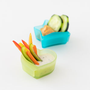 Bumkins Silicone Little Dipper Combo in Aqua Jelly, with veggie sticks & dip in heart-shaped bowl and cucumber slices on white.