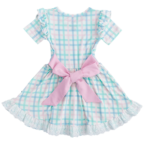 The Pastel Gingham Birdie Dress by Birdie Bean is crafted from plush bamboo viscose and features a pastel plaid in light blue, pink, and white checks. It boasts short sleeves, ruffled shoulders, a pink back bow, and a lacy white hem for comfort and charm.