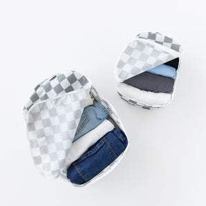 Bumkins Packing Cube 2 Pack: Charcoal Check sits open, holding neatly folded clothes, including denim, on a white background.