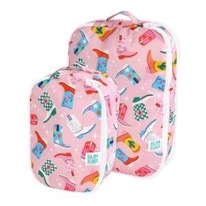 The Packing Cube 2 Pack: Boots by Bumkins includes two pink travel bags with colorful cowboy boots, white zippers, and waterproof fabric.