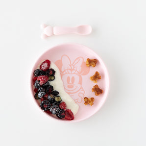 Bumkins Silicone Plate + Spoon Set: Disney Minnie Mouse features a pink dish with yogurt, berries, treats, and includes a training spoon and fork.