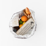 A Bumkins Packable Tote Bag: Lunar Phase holds eggs, an orange, a lime, cheese, and bread on a white backdrop.