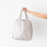 Someone holds the Bumkins Packable Tote Bag: Lunar Phase against a white brick wall.