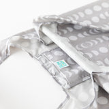 Close-up of a Bumkins Packable Tote Bag: Lunar Phase, featuring a gray fabric with white circular and crescent patterns. The glossy, waterproof material highlights its practicality.