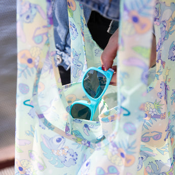 Close-up of a person putting blue sunglasses into a Bumkins Packable Tote Bag: Aloha Stitch.