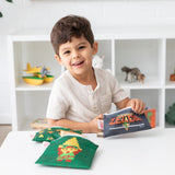 A young boy smiling with a Bumkins Reusable Snack Bag (3-Pack): The Legend of Zelda™, made of waterproof fabric, sits at a table.