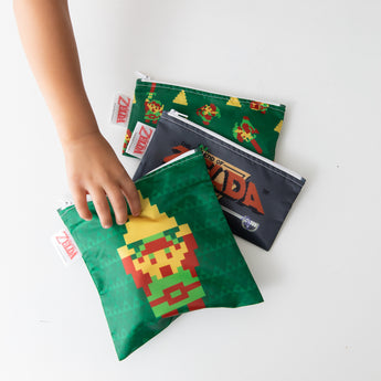 A child reaches for Bumkins Zelda-themed reusable snack bags featuring pixel art. Theyre machine washable and come in a 3-pack.