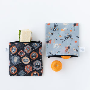 Bumkins Reusable Snack Bag, Large 2 Pack: Everyday Is Halloween beside two oranges, made from waterproof fabric with pumpkins and spooky designs.