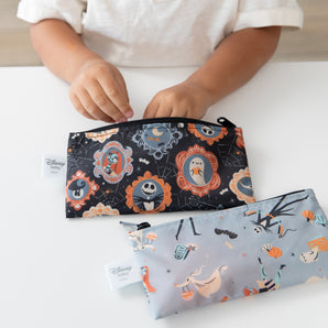 A child zips a Bumkins Everyday Is Halloween reusable snack bag with Disney characters on a table.