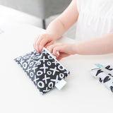 A child opens a Bumkins reusable snack bag, XOXO design, with a zipper on a white table.