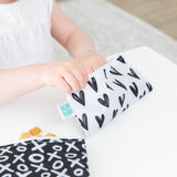 A child enjoys snacks from a Bumkins reusable snack bag with a black heart, while another has one adorned with XOXO.