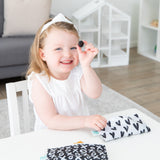 A girl in a white dress holds a blackberry at a table with Bumkins small reusable snack bags, XOXO & Hearts design.