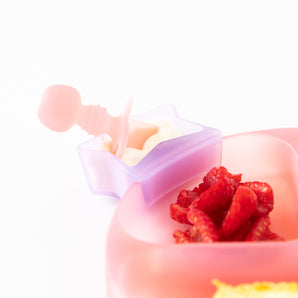 The purple container with a star lid holds Silicone Chewtensils®: Pink Jelly by Bumkins, ideal for baby weaning. Raspberries on pink surface.