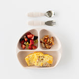 A divided plate with an omelette, fruit, and potatoes sits beneath the Bumkins Spoon + Fork: Sand on a white background.