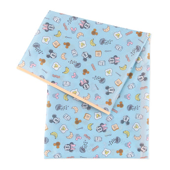 The Bumkins Splat Mat, Mickey + Minnie Sunny Side Up, features a light blue sheet set with playful cartoon characters, food items, and whimsical shapes like smiling faces and fruits. Its easy-cleaning design is perfect for achieving a Disney Splat Mat look.