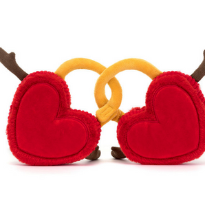 The Jellycat Amuseables Val & Tina Love Locks are plush red hearts with soft fur, linked by golden yellow locks. Each heart has brown arms in a welcoming gesture, set against a white background.