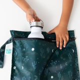 A child places a white water bottle into the Bumkins Wet Bag: Starry Cactus on a white table.