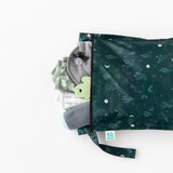 The Bumkins Wet Bag: Starry Cactus, in dark green with cactus patterns and waterproof fabric, is partially open on a white background, revealing baby items including a gray cap, pacifier, and cactus-patterned clothing.