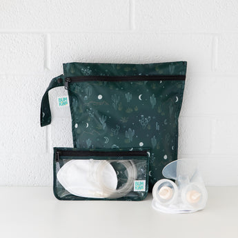 Bumkins Wet Bag: Starry Cactus sits against a white brick wall with a breast pump and nursing accessories in front.