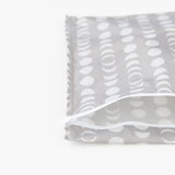 The Bumkins Wet Bag: Lunar Phase features a gray fabric with white dot and circle patterns, resembling a lunar cycle. It has a partially open white zipper and is crafted from waterproof fabric with heat-sealed seams, offering durability. Its minimalist design stands out against the white background.