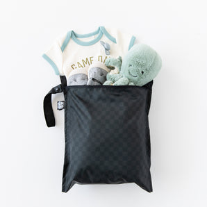 Bumkins Rich Black Wet Bag with a baby onesie, gray shoes, and a green stuffed octopus peeking out.