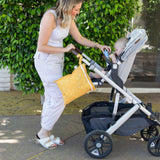 Woman in white gives baby a drink next to stroller carrying Bumkins Wet Bag: Sunshine on a sunny day.