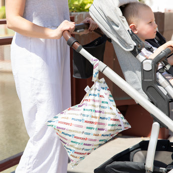 A person pushes a stroller with a toddler, a Bumkins Wet Bag: Mickey & Friends Varsity hanging from the handle.