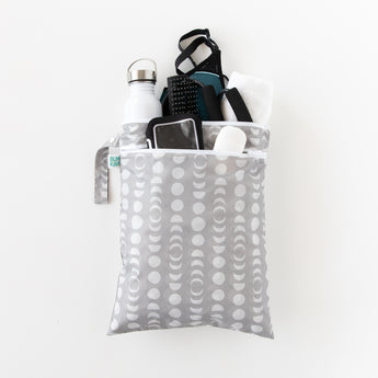 The Bumkins Wet/Dry Bag: Lunar Phase, featuring a gray and white pattern, is made from waterproof fabric to hold items like a water bottle, phone, towel, and sunglasses. This versatile organizer bag has a zipper and handle and is elegantly displayed against a plain white background.