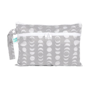 The Bumkins Wet/Dry Clutch: Lunar Phase is gray with white crescent moon shapes, crafted from waterproof fabric. It features a snap handle for convenience and has a Bumkins label on the side.