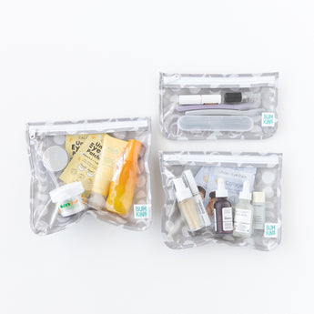 Three clear travel bags from Bumkins Clear Travel Bag 3 Pack: Lunar Phase, filled with skincare products on a white background.