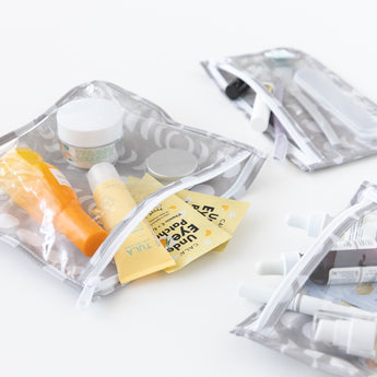 Bumkins Lunar Phase Clear Travel Bag 3 Pack filled with skincare sachets and toiletries on a white background.