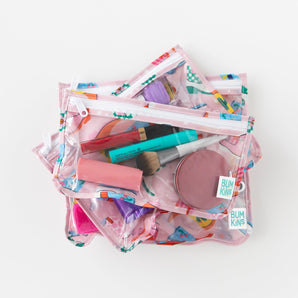 Three transparent pink Bumkins makeup bags, with vibrant designs, are TSA-compliant and ideal for travel cosmetics.