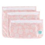 The Clear Travel Bag 3-Pack: Lace by Bumkins includes three pink floral-patterned zippered pouches, ideal for travel. Each pouch features a white zipper and one displays the BUMKINS logo at the bottom right corner. They are stacked slightly offset from each other.