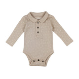 The Organic Polo Bodysuit by Lovedbaby in Oatmeal Dots is made from organic cotton with a Peter Pan collar, long sleeves, and button placket. It features a subtle white floral pattern, bottom snap closures for easy changing, and uses eco-friendly dyes to ensure sustainability.